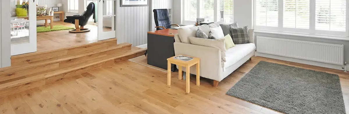 A modern living room with professionally installed laminate flooring, a beige sofa, a small side table, a gray rug, and large windows with white shutters in Las Vegas, NV